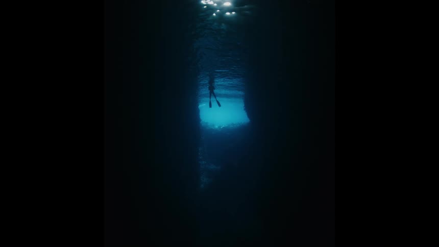 A diver's silhouette is framed by the sparkling surface light, viewed from the dark depths of an underwater cave