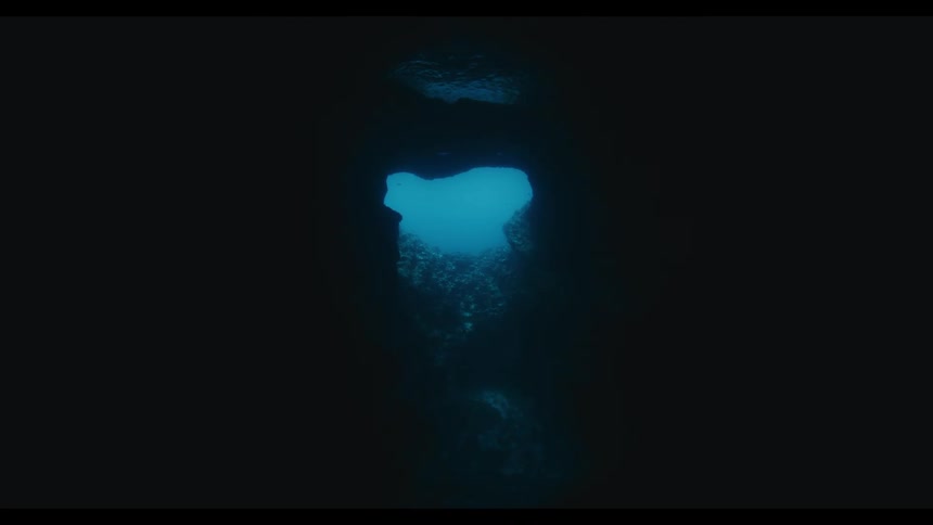 A slow zoom towards a heart-shaped opening in a dark underwater cave reveals the bright blue ocean surface