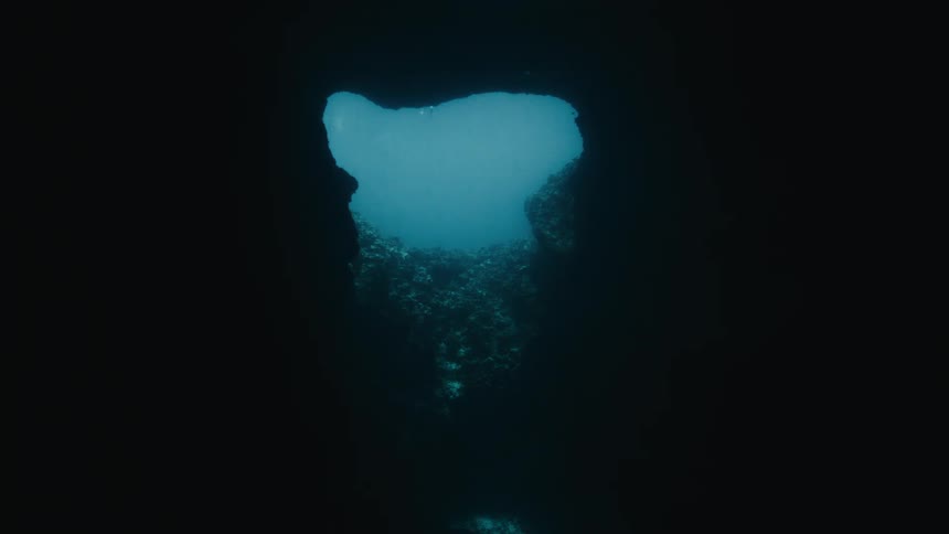 Slow zoom out from a dark underwater cave reveals a bright blue opening to the ocean