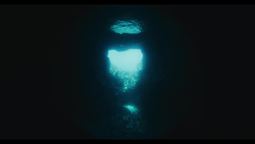 A tranquil view from inside a dark underwater cave looking up towards a bright opening to the sea