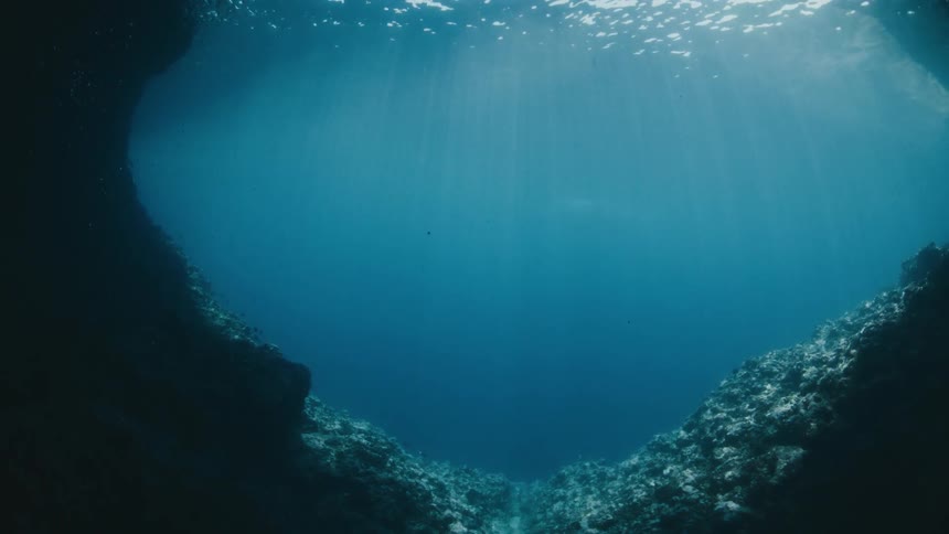 A serene underwater view from a dark cave looking up towards a heart-shaped opening where sunlight beams through the blue ocean surface