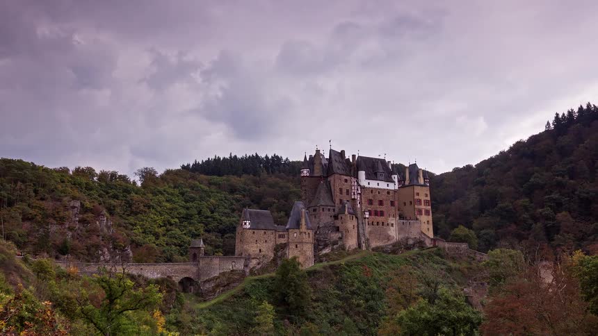 A dramatic timelapse of the historic Eltz Castle in Germany, nestled in a forested valley under a cloudy sky