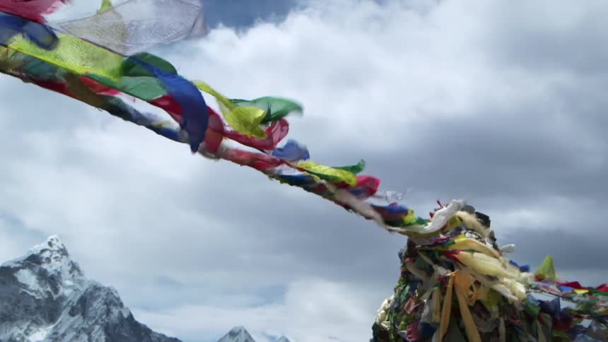 Colorful flags on ropes waving in the wind in front of snow covered mountains