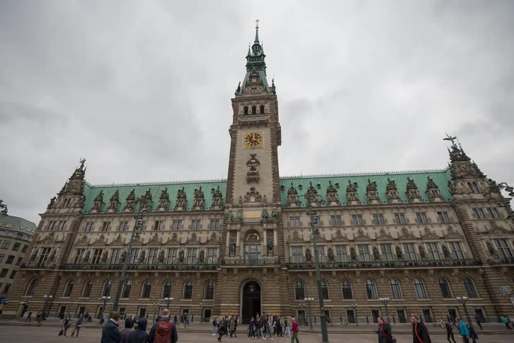 A slow-motion timelapse reveals the grand architecture of Hamburg City Hall as people walk through the bustling Rathausmarkt square on an overcast day