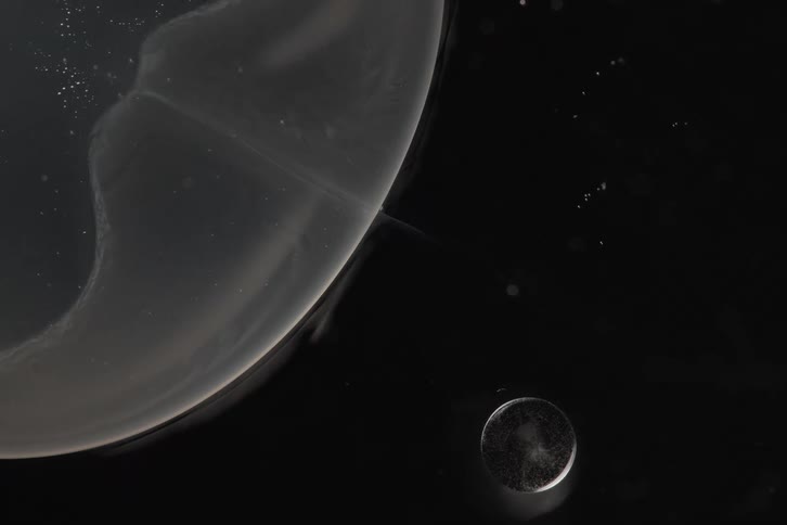 An abstract macro shot of milky planets and dust particles floating slowly through the dark void of space