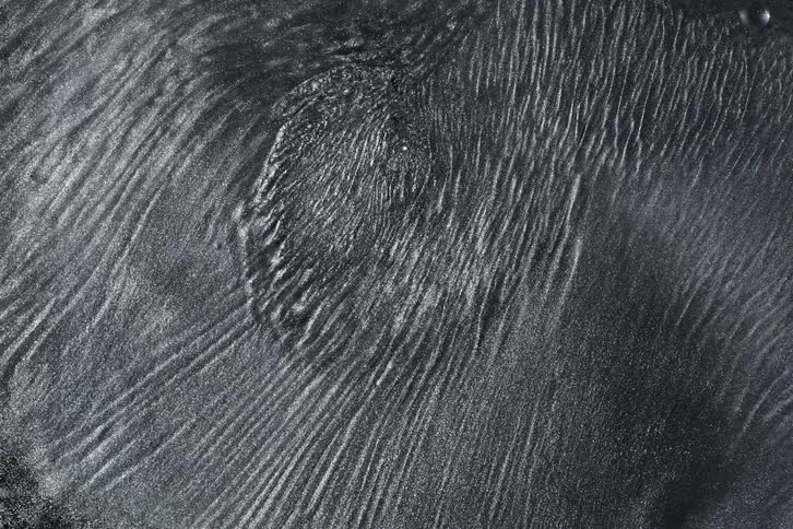 A mesmerizing macro shot of a dark, shimmering viscous fluid slowly rippling and creating intricate linear patterns