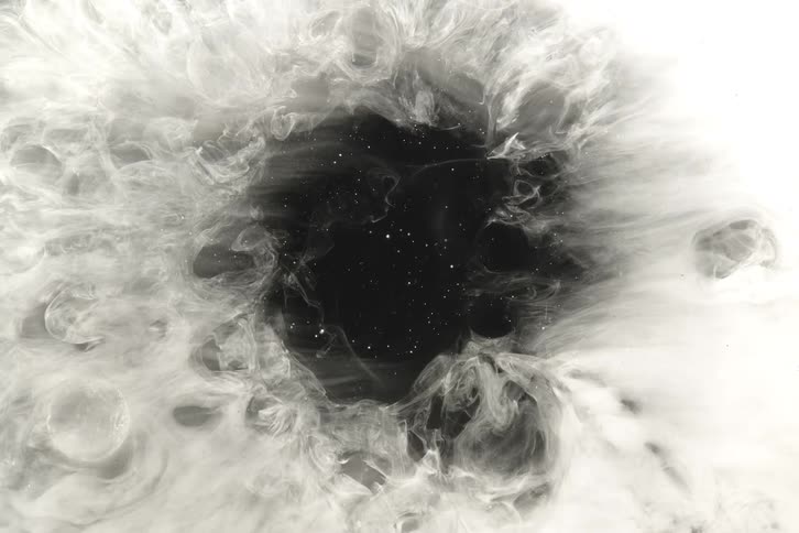 A cosmic black hole filled with stars is revealed as ethereal white smoke swirls and expands outwards