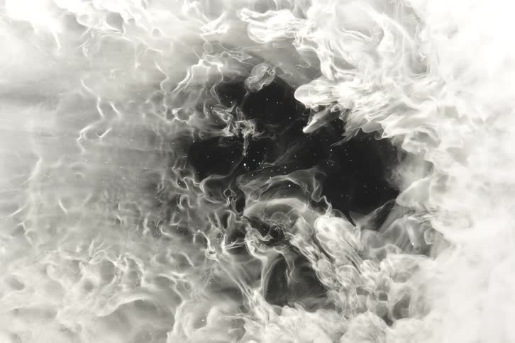 Ethereal white ink expands and creates intricate, smoke-like textures against a dark background in slow motion
