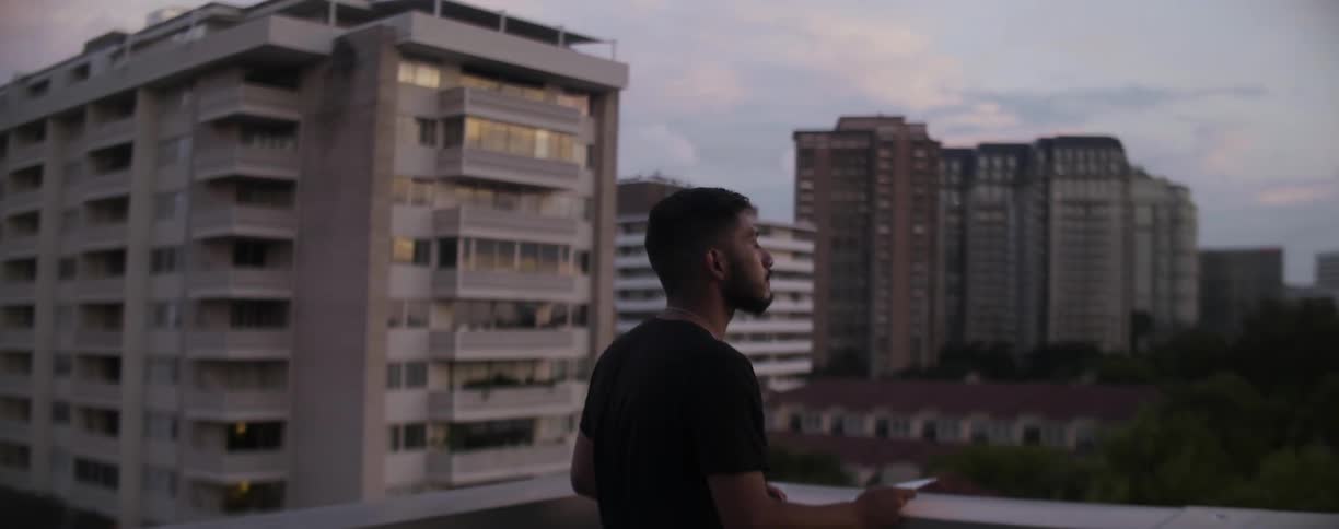 A man stands on a rooftop overlooking a city