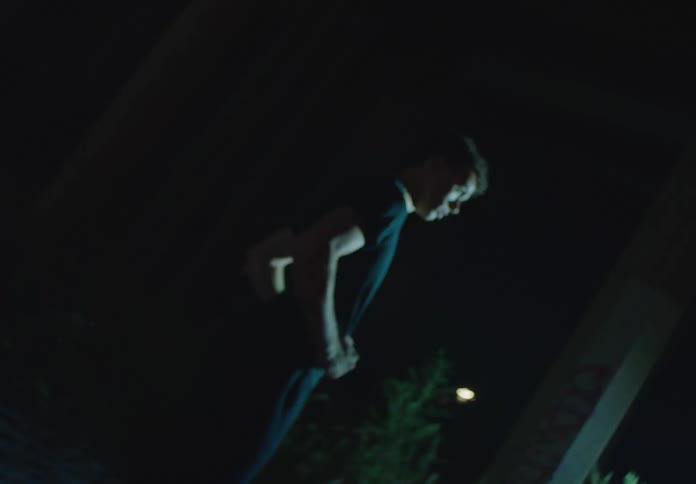 An energetic young man performs an expressive dance under a city overpass at night with dramatic lighting and lens flares
