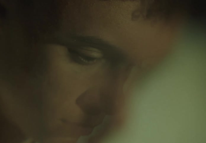 Intense close-up on a young man's focused eye as colored lights from a screen flicker across his face in the dark
