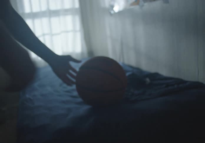 A determined young athlete puts on his shirt, grabs his basketball from his bed, and leaves his room