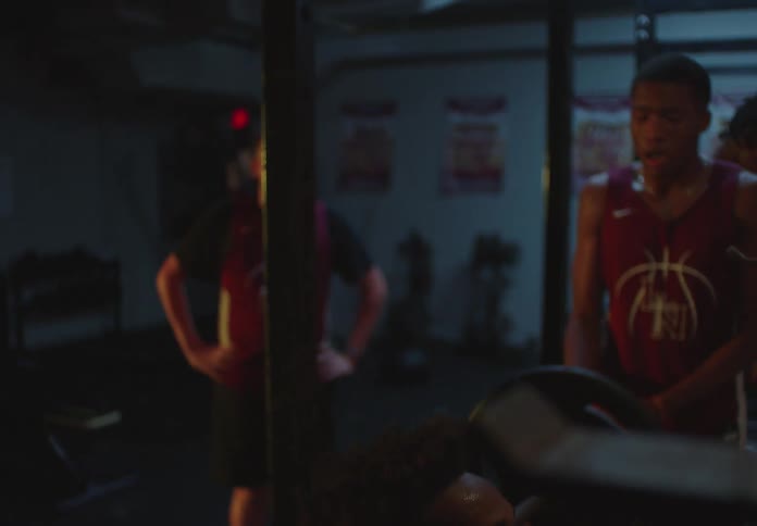 Close up of a determined young athlete doing heavy squats with a barbell in a dimly lit gym