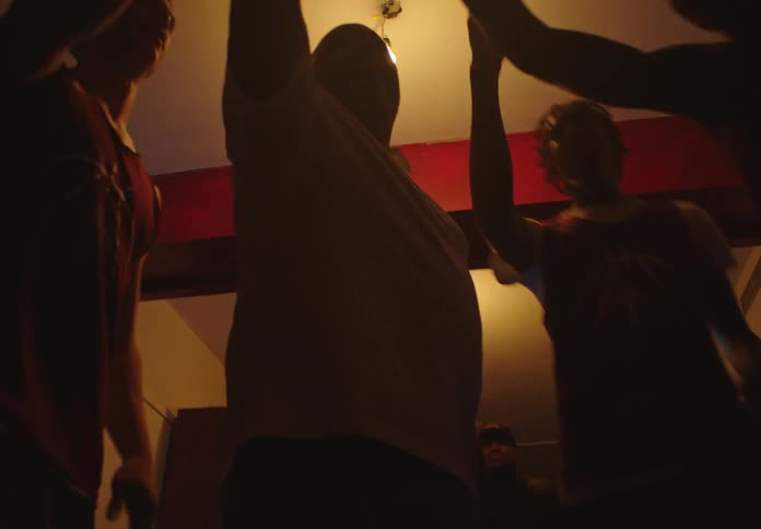 A basketball team huddles with their coach in a dark locker room, getting motivated and putting their hands in together before a game