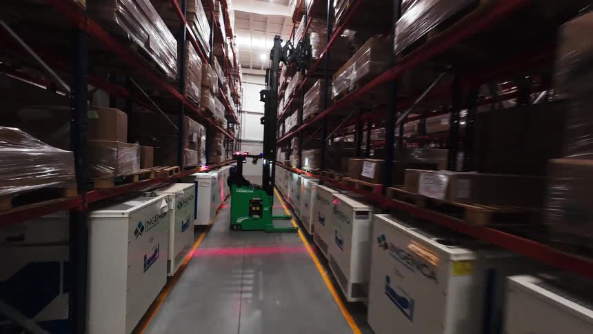 A POV shot from a forklift driving down a narrow aisle in a large, modern logistics warehouse filled with inventory