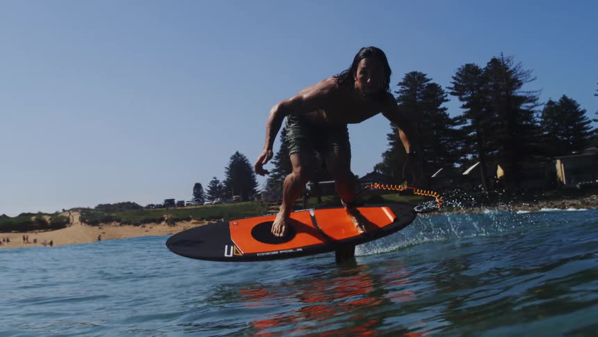A long-haired surfer intensely glides over the water on an electric hydrofoil surfboard in stunning slow motion