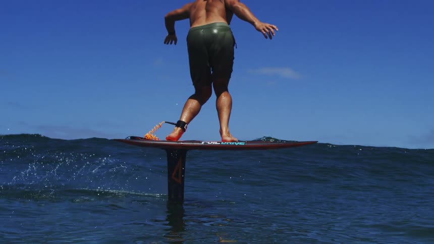 A skilled surfer gracefully carves through the ocean on an electric hydrofoil surfboard in stunning slow motion