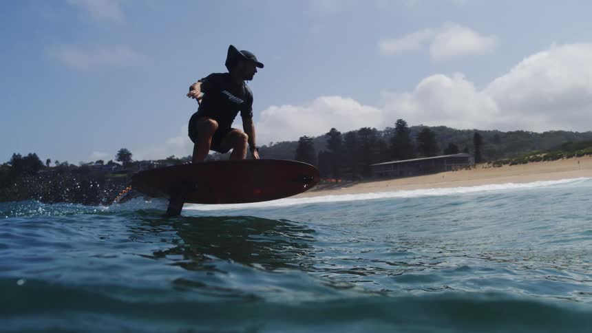 A man skillfully glides across the tranquil ocean waves on an electric hydrofoil surfboard in mesmerizing slow motion