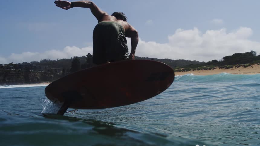 A skilled male surfer glides gracefully on a hydrofoil surfboard across the ocean waves in dramatic slow motion