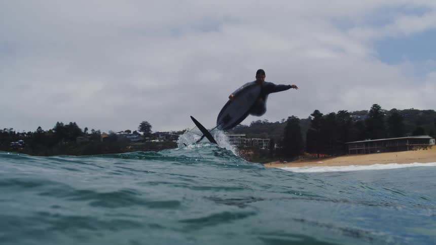 A hydrofoil surfer performs an impressive aerial jump off a wave in dramatic super slow motion