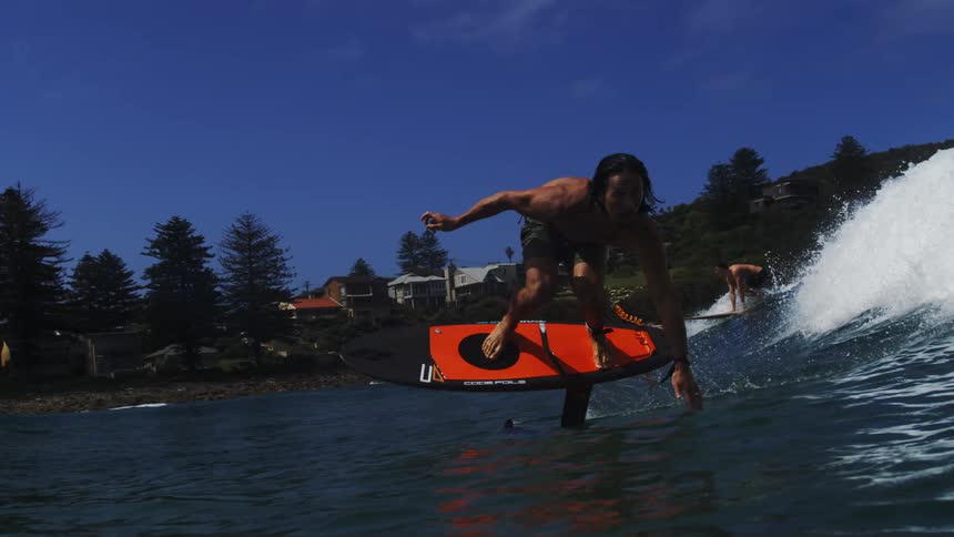 A surfer gracefully rides a hydrofoil board on a breaking wave in super slow motion on a sunny day