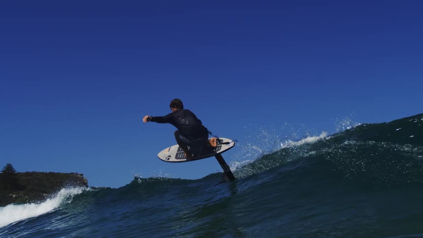 A skilled surfer gracefully carves along a beautiful blue ocean wave on a hydrofoil surfboard in super slow motion