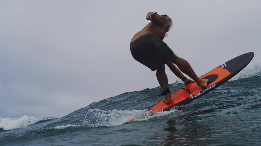 A skilled surfer gracefully rides a large ocean wave on a hydrofoil surfboard in dramatic slow motion before launching into the air
