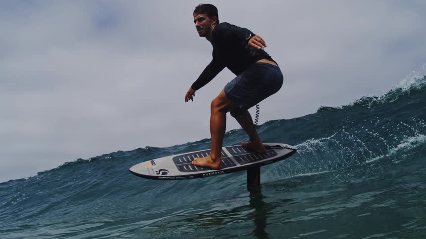 A male hydrofoil surfer skillfully rides a breaking ocean wave in dramatic super slow motion as the camera follows alongside before being overtaken by the water