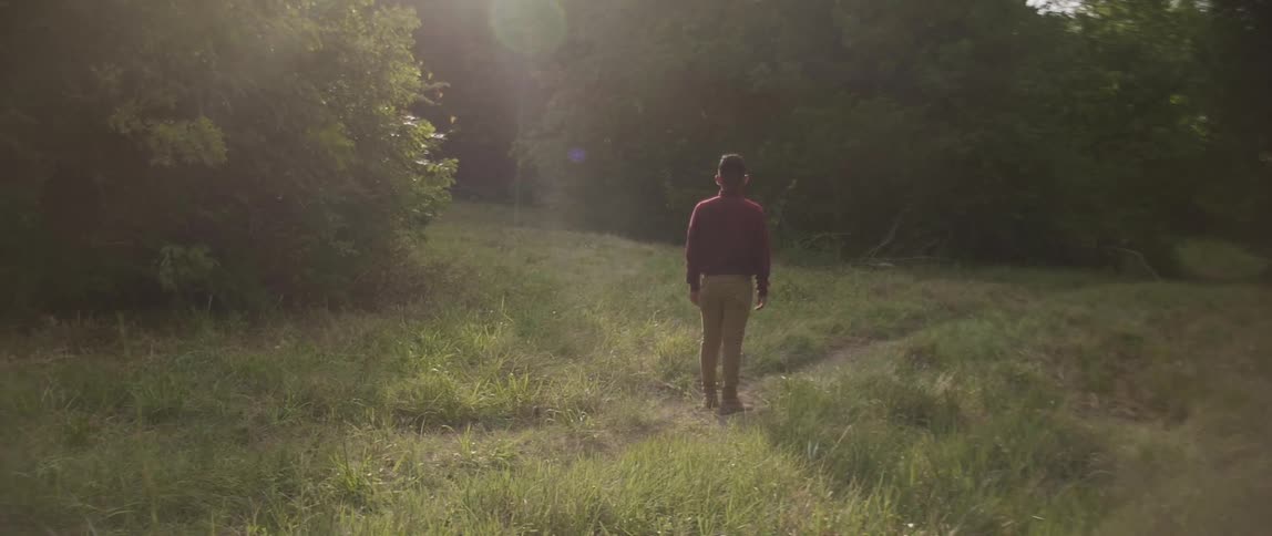 A man is walking on a field near the woods