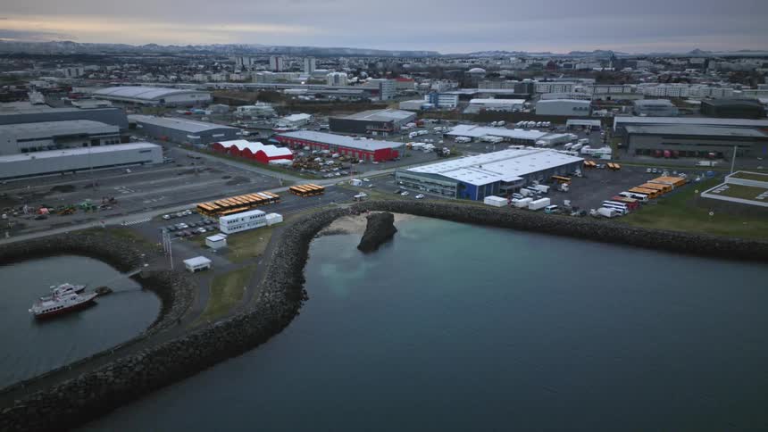 A still aerial view shows the industrial port area of a city with warehouses and a small harbor under an overcast sky