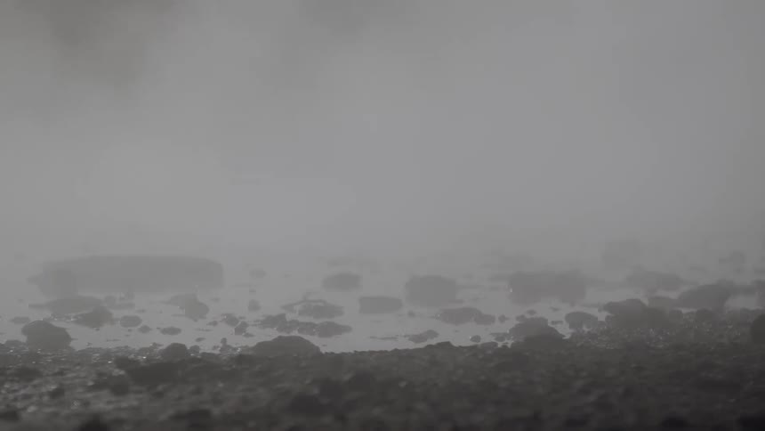 Thick steam billows over a rocky geothermal landscape, creating a mysterious and foggy atmosphere