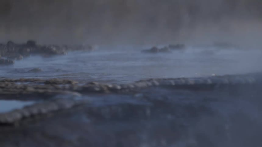 Wispy steam gently rises from the surface of a tranquil geothermal hot spring