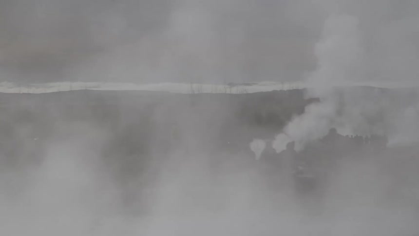 Thick white steam billows across a geothermal landscape, slowly revealing the silhouettes of tourists watching a geyser