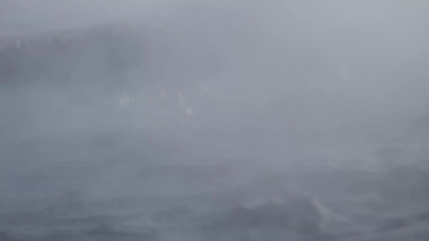 An intense close-up of dark, turbulent water with heavy mist and sea smoke blowing across the churning waves during a storm