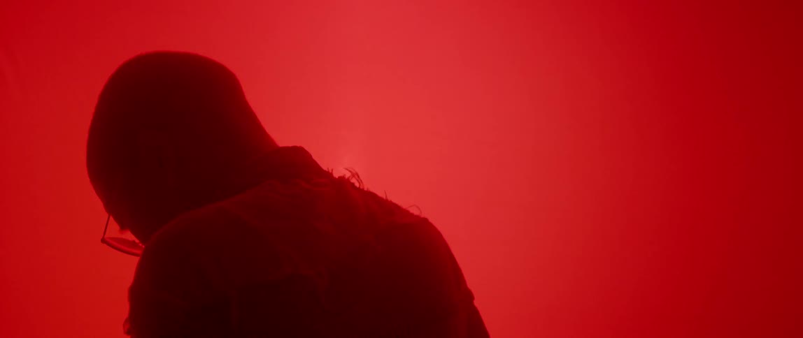 A person with a shaved head and glasses standing in a room with a bright red light