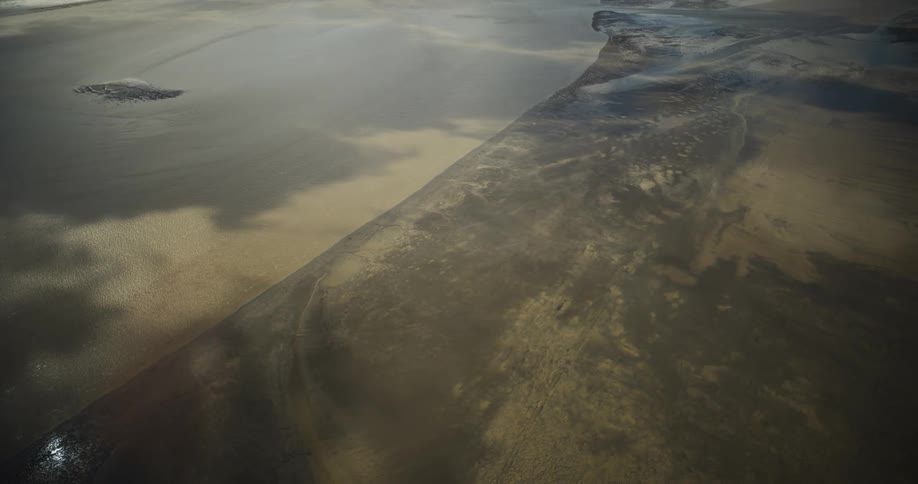 Atmospheric shot of fine sand blowing like mist across a vast, dark, and desolate wet beach