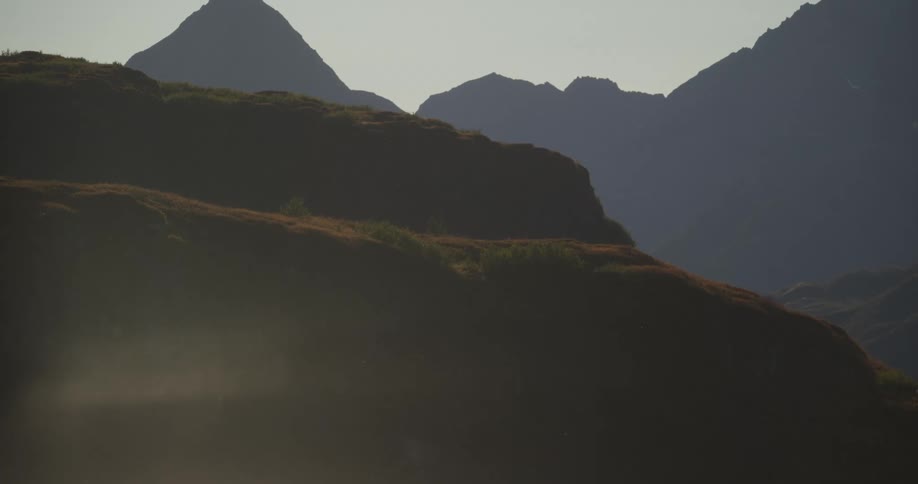 Sunlight catches tiny floating particles in the air above a hazy, silhouetted mountain range at dawn