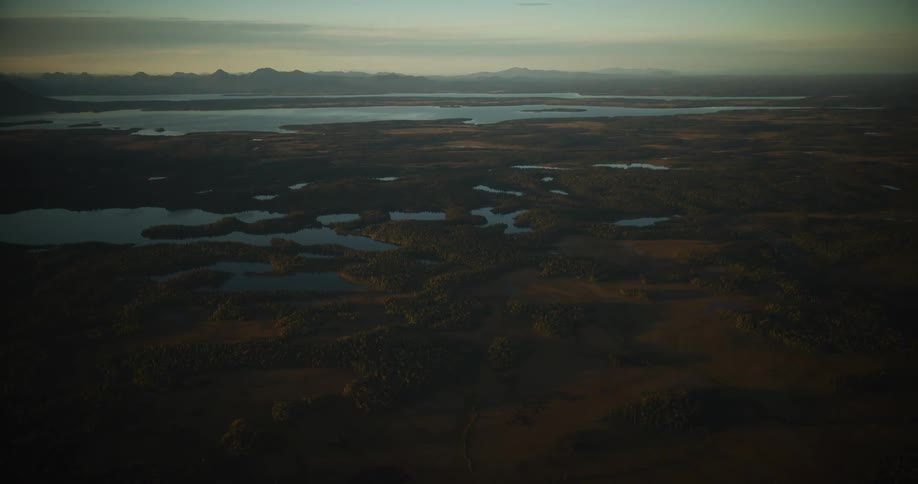 An expansive aerial view reveals a remote wilderness dotted with shimmering lakes and dense forests under a soft, dusky sky