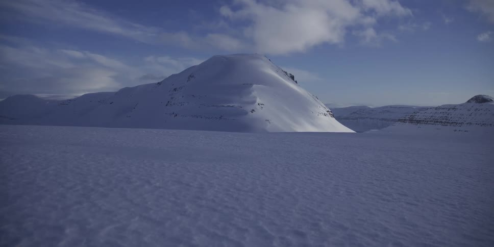 A majestic, snow-covered mountain stands tall over a vast, frozen plain under a clear blue sky
