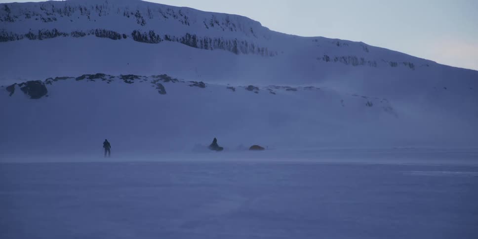 An arctic explorer stands in a blizzard while camping in a vast, desolate, and snowy landscape