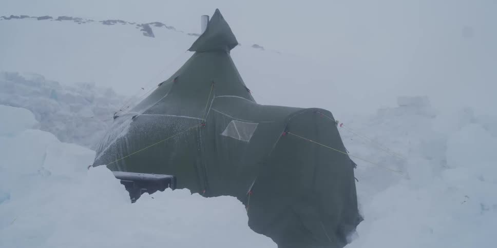 A survival tent is battered by high winds and blowing snow during a blizzard in a remote arctic landscape