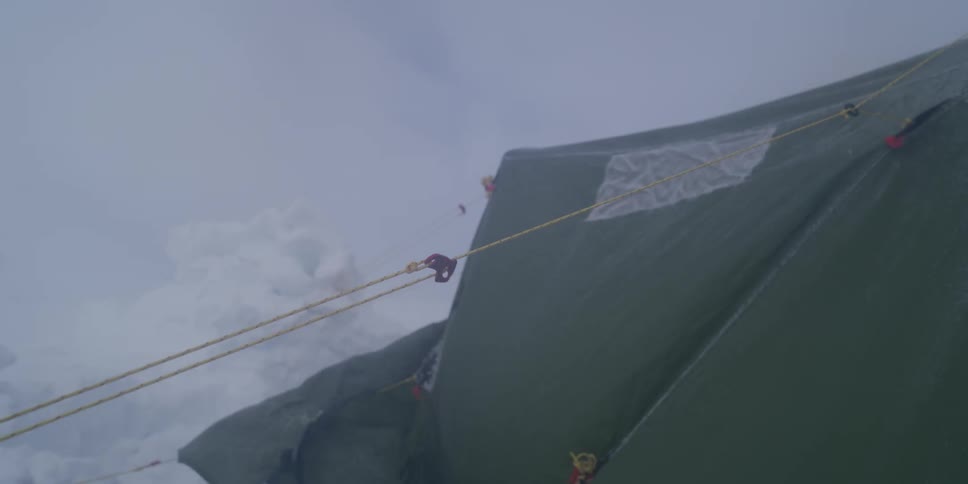 A green expedition tent is battered by high winds and blowing snow during a blizzard on a mountain