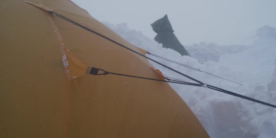 A sturdy yellow tent is battered by heavy winds and blowing snow during an intense blizzard at a mountain base camp