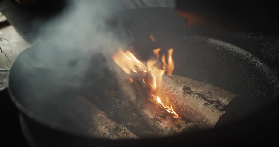 Close up slow motion of birch logs igniting and burning in a dark metal fire pit