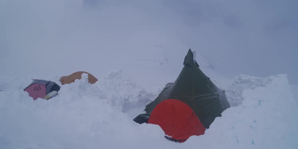 A high-altitude mountaineering camp with colorful tents is battered by extreme weather conditions during a fierce snowstorm