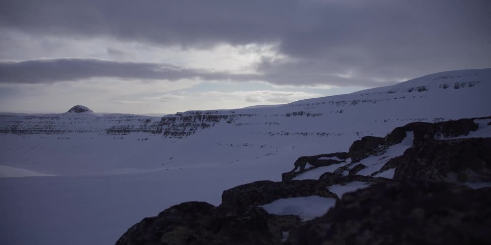 Slow dolly shot reveals an immense, snow-covered valley and mountain range under a cloudy sky