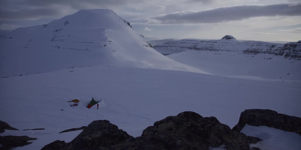 A remote campsite is nestled in a vast, snow-covered mountain valley during winter