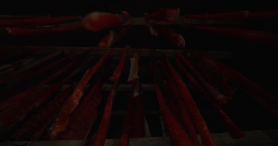 Looking up at long red strips of salmon hanging to cure in a dark, traditional smokehouse