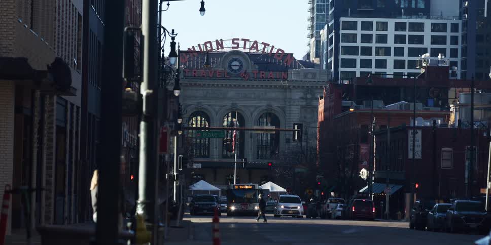 Sunlight illuminates the historic Union Station in downtown Denver as traffic and pedestrians move along the city streets