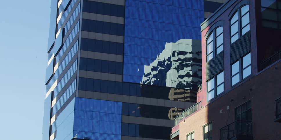 A close-up of a modern blue glass office building with a distorted reflection of a city building